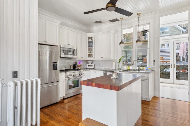 kitchen with appliances with stainless steel finishes, white cabinets, wooden counters, and radiator heating unit