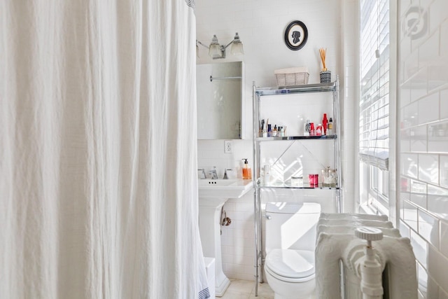 bathroom with toilet, a sink, backsplash, and tile walls