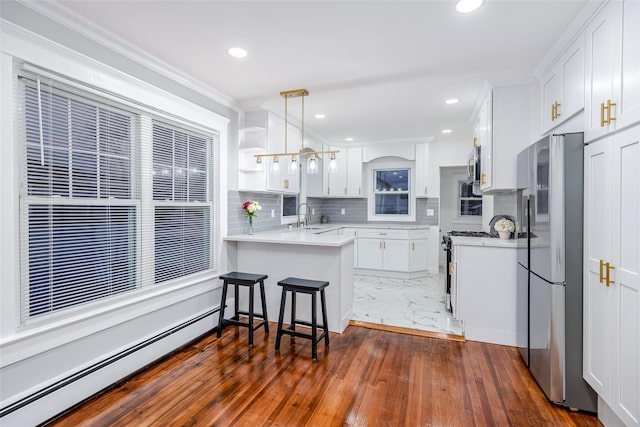 kitchen featuring white cabinets, appliances with stainless steel finishes, a peninsula, baseboard heating, and a sink