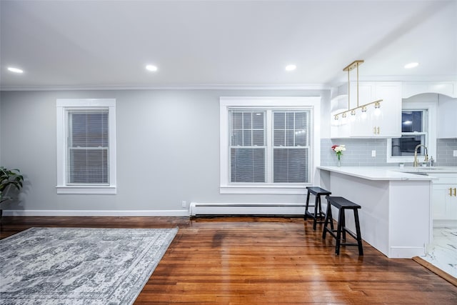 kitchen featuring a breakfast bar, tasteful backsplash, a baseboard heating unit, white cabinetry, and a sink