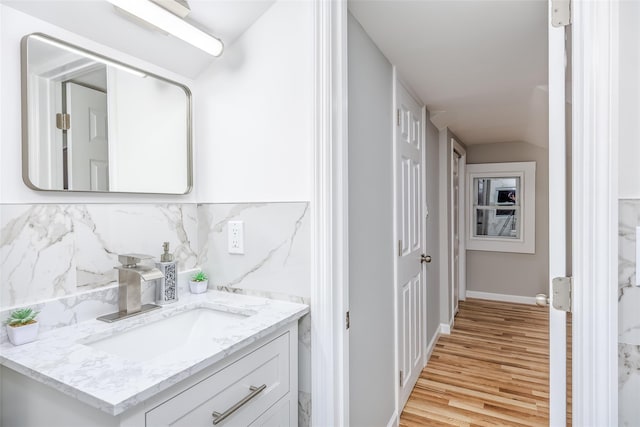 bathroom featuring wood finished floors, vanity, baseboards, vaulted ceiling, and decorative backsplash