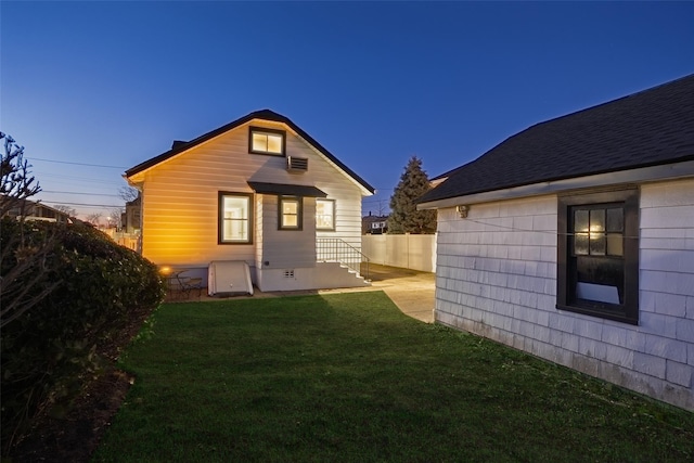 back of property at dusk with a yard, crawl space, and fence