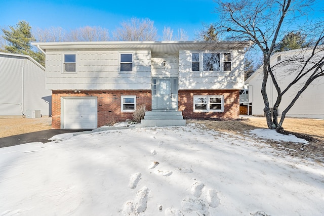 raised ranch featuring a garage, brick siding, and central AC