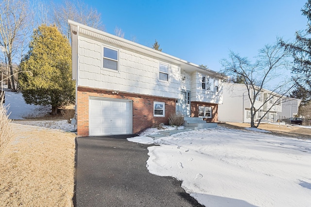 raised ranch with brick siding, an attached garage, and aphalt driveway