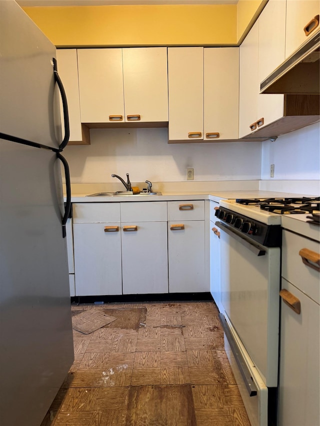 kitchen featuring under cabinet range hood, a sink, white cabinetry, freestanding refrigerator, and gas range gas stove