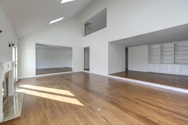 unfurnished living room with built in features, a skylight, a high end fireplace, wood finished floors, and high vaulted ceiling