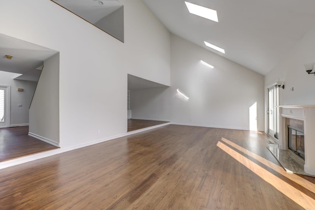 unfurnished living room featuring a skylight, baseboards, wood finished floors, a fireplace, and high vaulted ceiling