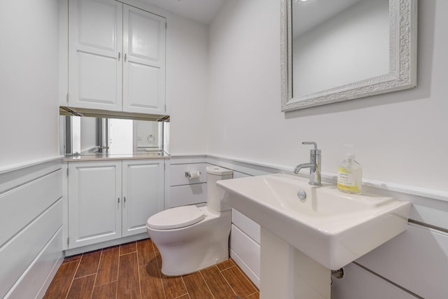 bathroom with wood finish floors, a wainscoted wall, a sink, and toilet