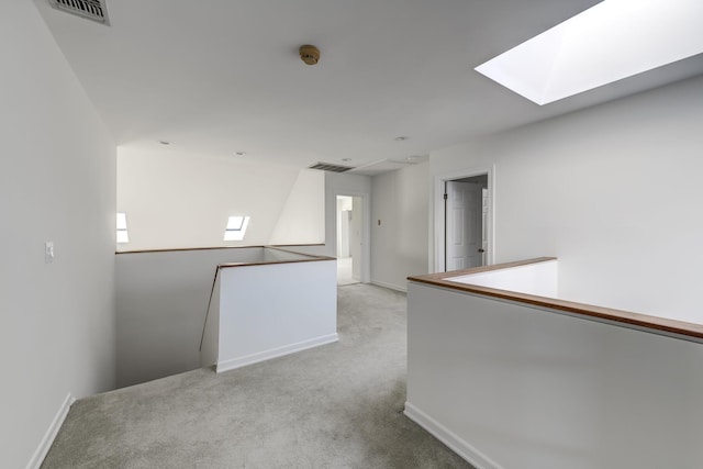 unfurnished room with light carpet, a skylight, baseboards, and visible vents