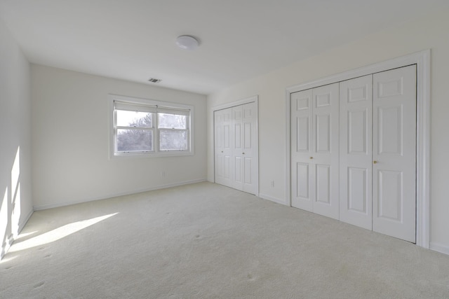 unfurnished bedroom with baseboards, visible vents, two closets, and carpet flooring