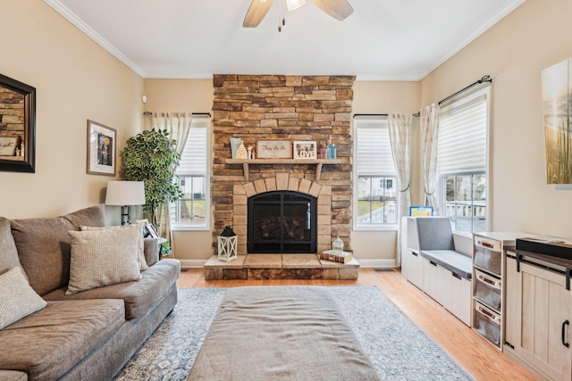 living room with a fireplace, a ceiling fan, baseboards, ornamental molding, and light wood finished floors