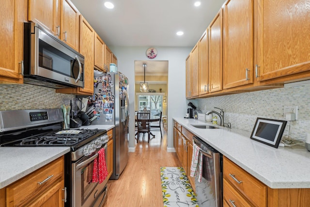 kitchen featuring stainless steel appliances, decorative backsplash, a sink, light wood-type flooring, and baseboards