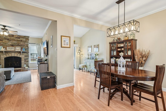 dining space with light wood-style flooring, a fireplace, a ceiling fan, baseboards, and crown molding