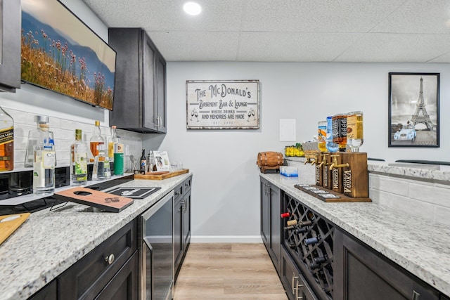 kitchen featuring light wood finished floors, baseboards, decorative backsplash, a drop ceiling, and light stone countertops