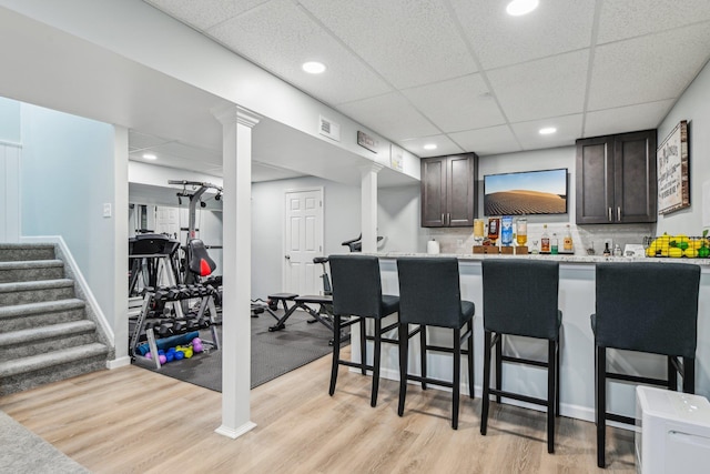 bar featuring tasteful backsplash, a paneled ceiling, visible vents, stairway, and light wood-style floors