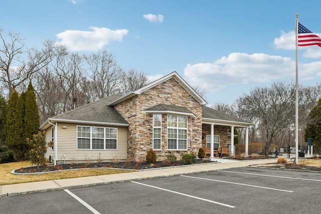 view of front facade featuring uncovered parking, stone siding, and roof with shingles