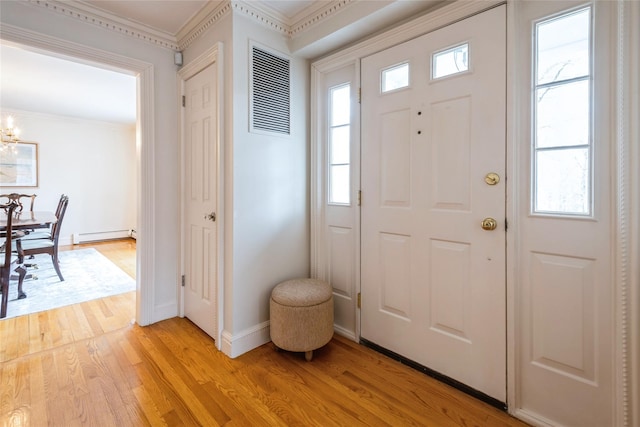 foyer entrance featuring a baseboard heating unit, baseboards, ornamental molding, light wood-type flooring, and an inviting chandelier