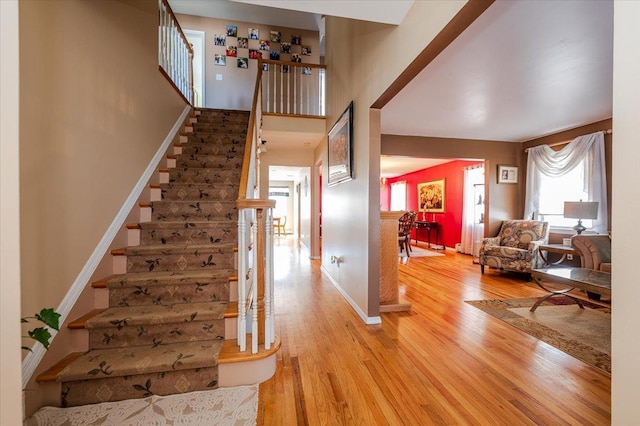 stairway featuring a towering ceiling, baseboards, and wood finished floors