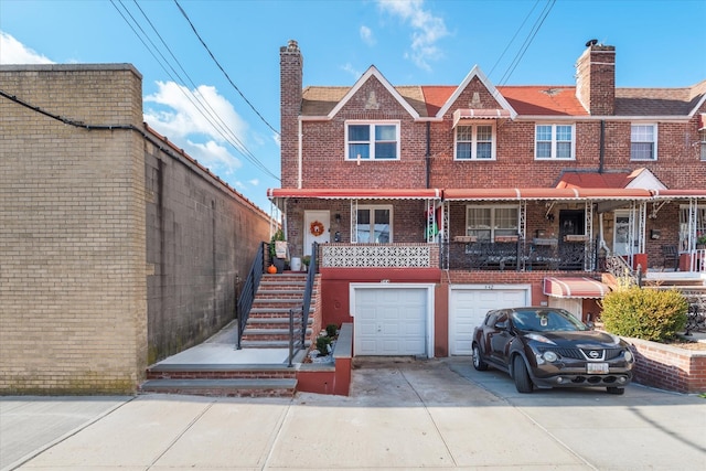 view of property featuring brick siding, driveway, a chimney, and an attached garage