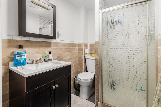 bathroom featuring toilet, a wainscoted wall, vanity, tile walls, and a stall shower