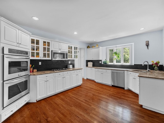 1 Finnegan Ln, Montebello, NY 10901 - kitchen featuring appliances with stainless steel finishes, glass insert cabinets, tasteful backsplash, dark wood-type flooring, and white cabinets