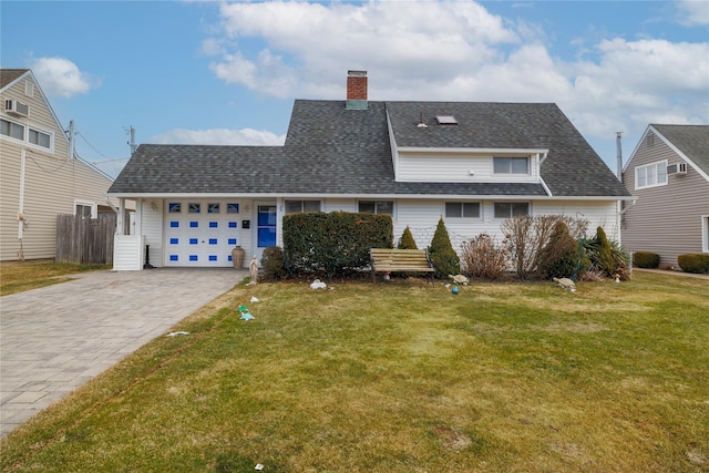 view of front facade with decorative driveway, roof with shingles, a chimney, an attached garage, and a front yard