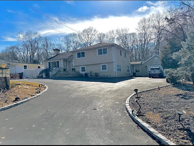 tri-level home featuring a chimney, fence, aphalt driveway, and stucco siding