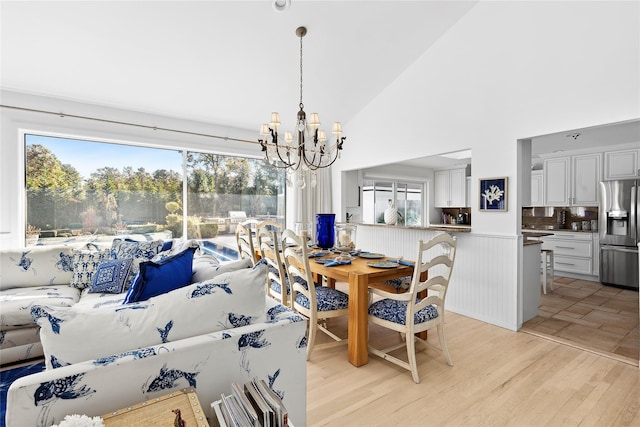 dining room with high vaulted ceiling, a notable chandelier, and light wood-style flooring