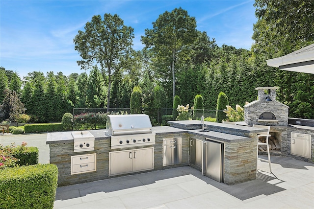 view of patio / terrace featuring an outdoor stone fireplace, fence, grilling area, and an outdoor kitchen