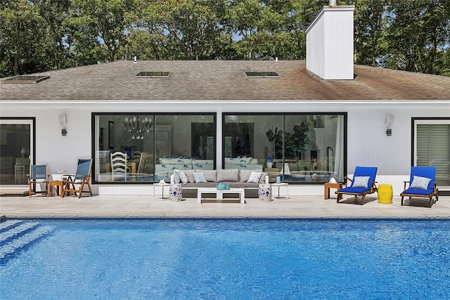 back of property with a patio area, a shingled roof, and an outdoor pool