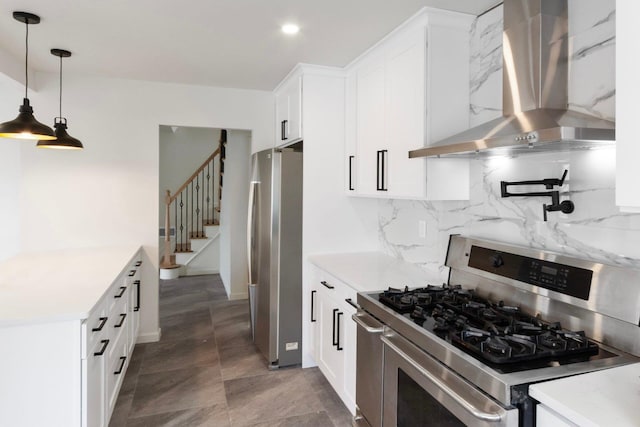 kitchen featuring white cabinetry, hanging light fixtures, wall chimney range hood, appliances with stainless steel finishes, and backsplash