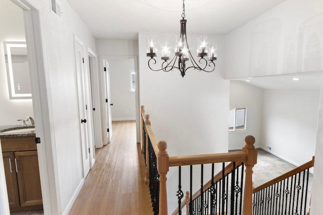 corridor with visible vents, light wood finished floors, a sink, and an upstairs landing