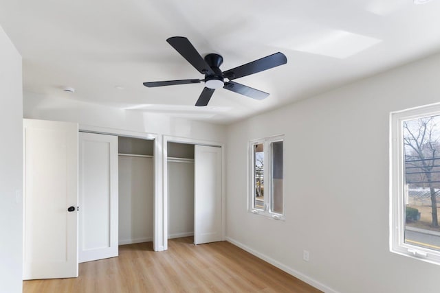 unfurnished bedroom featuring baseboards, light wood-type flooring, a ceiling fan, and multiple closets