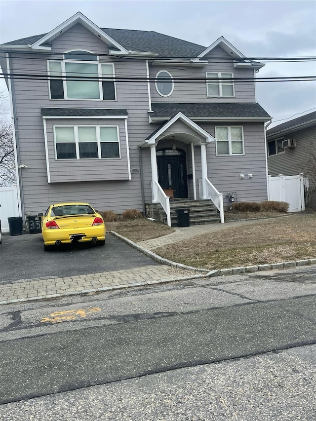 view of front of house featuring a shingled roof, fence, and aphalt driveway