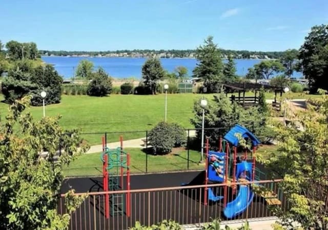 community jungle gym with fence, a lawn, and a water view