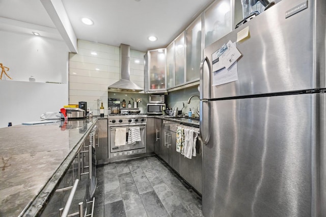 kitchen featuring decorative backsplash, stainless steel appliances, wall chimney range hood, a sink, and recessed lighting