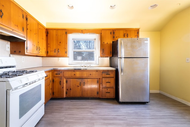 kitchen with white range with gas stovetop, a sink, light wood-style floors, light countertops, and freestanding refrigerator