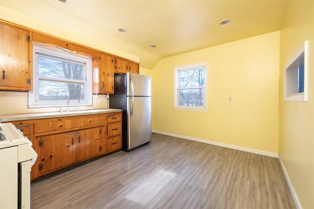 kitchen with stove, brown cabinetry, freestanding refrigerator, a sink, and baseboards