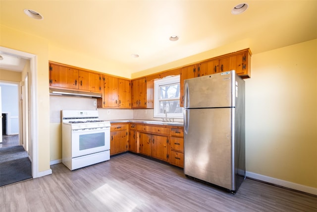 kitchen with brown cabinetry, freestanding refrigerator, light countertops, under cabinet range hood, and gas range gas stove