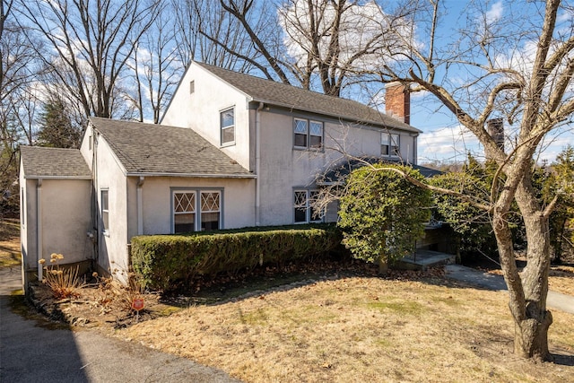 exterior space with roof with shingles, a chimney, and stucco siding