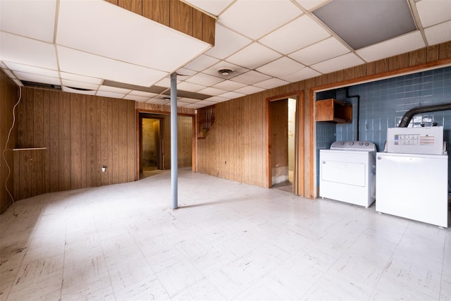 finished basement with a paneled ceiling, wooden walls, separate washer and dryer, and tile patterned floors