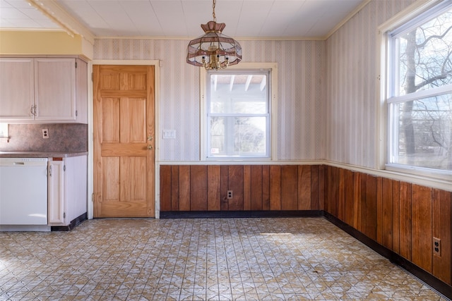 unfurnished dining area with wallpapered walls, a wainscoted wall, ornamental molding, light floors, and a chandelier