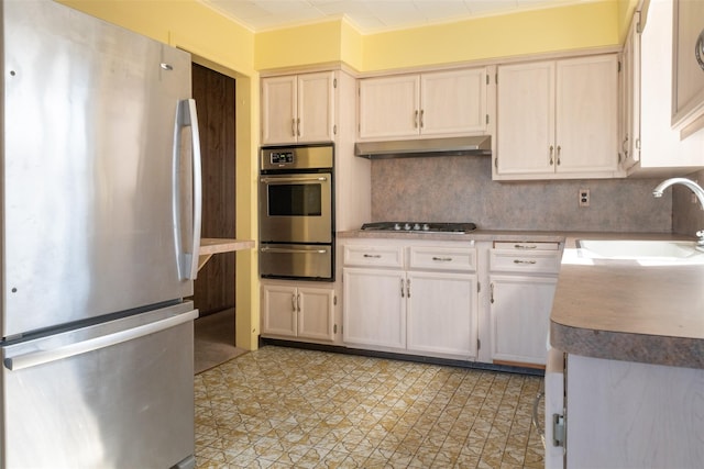 kitchen featuring a warming drawer, decorative backsplash, appliances with stainless steel finishes, a sink, and under cabinet range hood