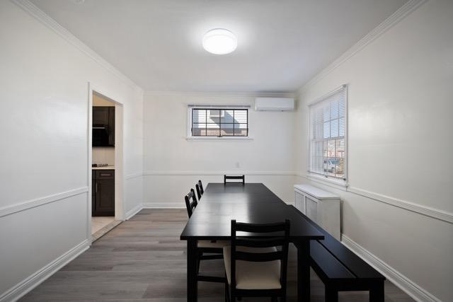 dining room featuring a wall unit AC, wood finished floors, baseboards, and ornamental molding