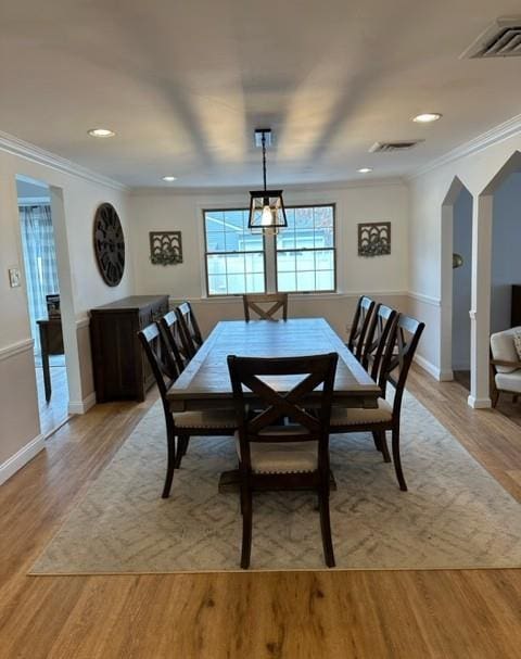 dining space with ornamental molding, arched walkways, visible vents, and light wood finished floors