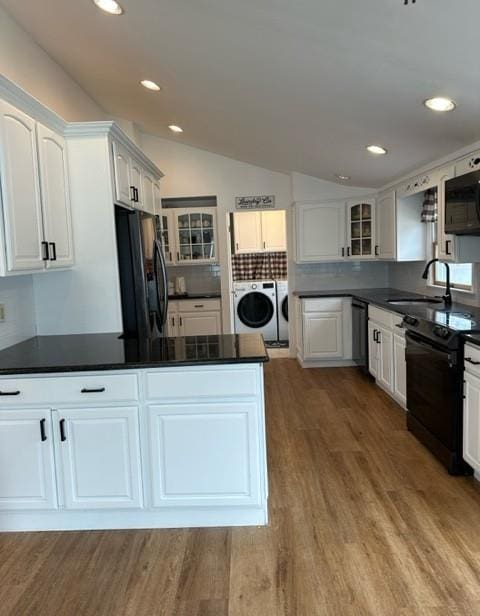 kitchen featuring dark countertops, glass insert cabinets, black appliances, washing machine and dryer, and a sink