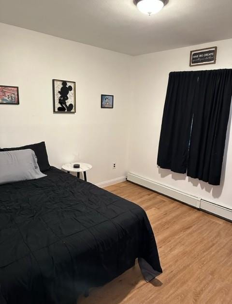 bedroom with baseboards, a baseboard heating unit, and wood finished floors