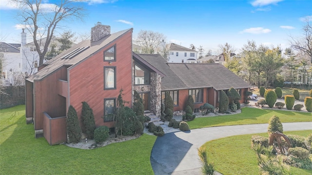 view of front facade with curved driveway, a chimney, a front yard, and a shingled roof