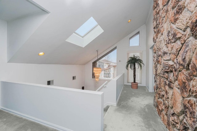 hall with visible vents, lofted ceiling with skylight, carpet, and an upstairs landing