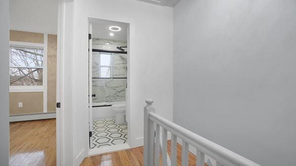 hallway featuring an upstairs landing, baseboard heating, and wood finished floors